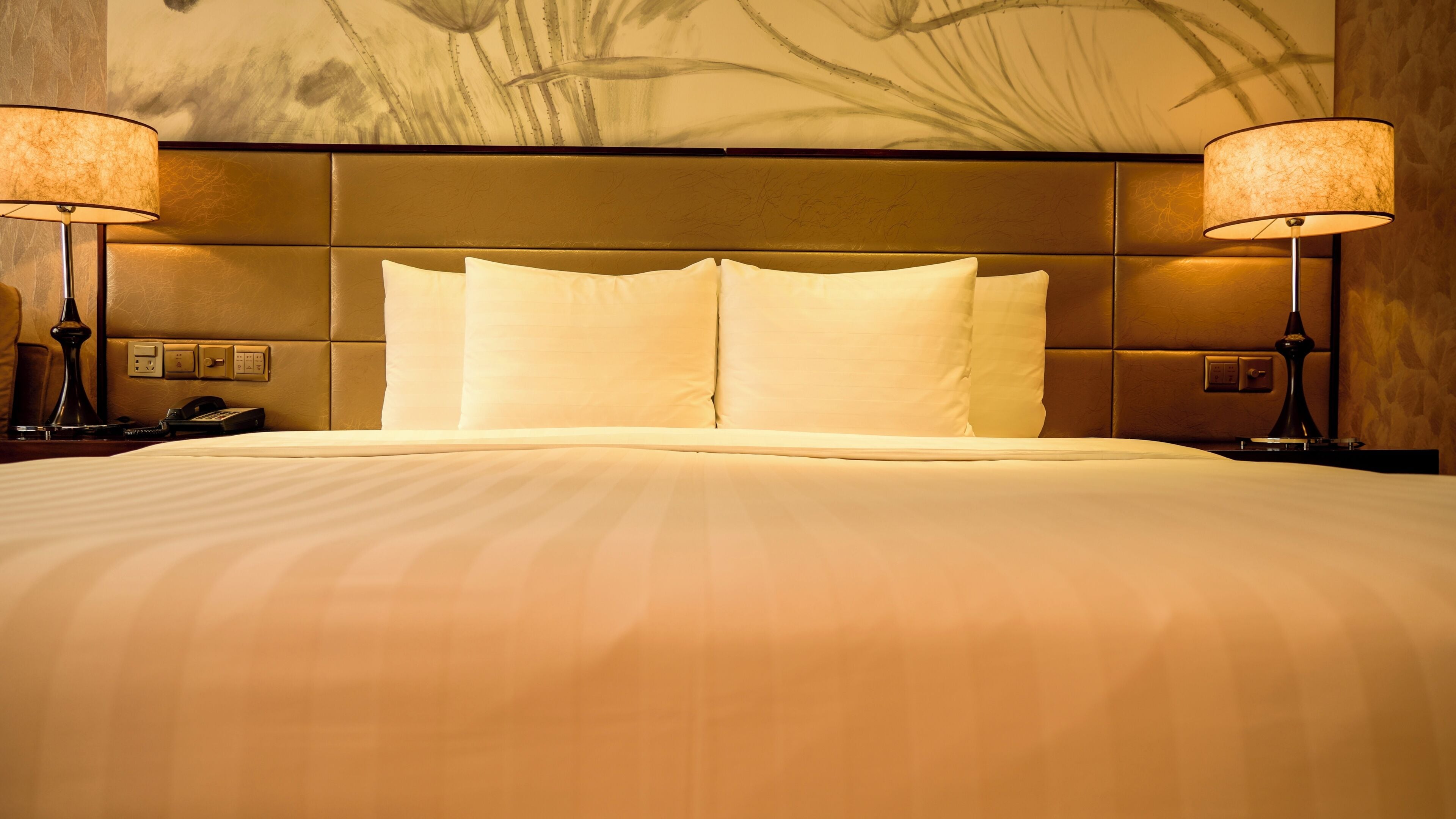 A hotel room with a large bed, two bedside lamps, a telephone, and a wall with a floral pattern.