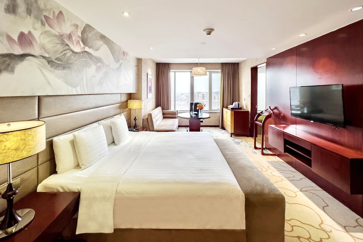 Ein Hotelzimmer mit einem großen Bett, einem Fernseher, einer Couch, einem Schreibtisch und einem Bild an der Wand.