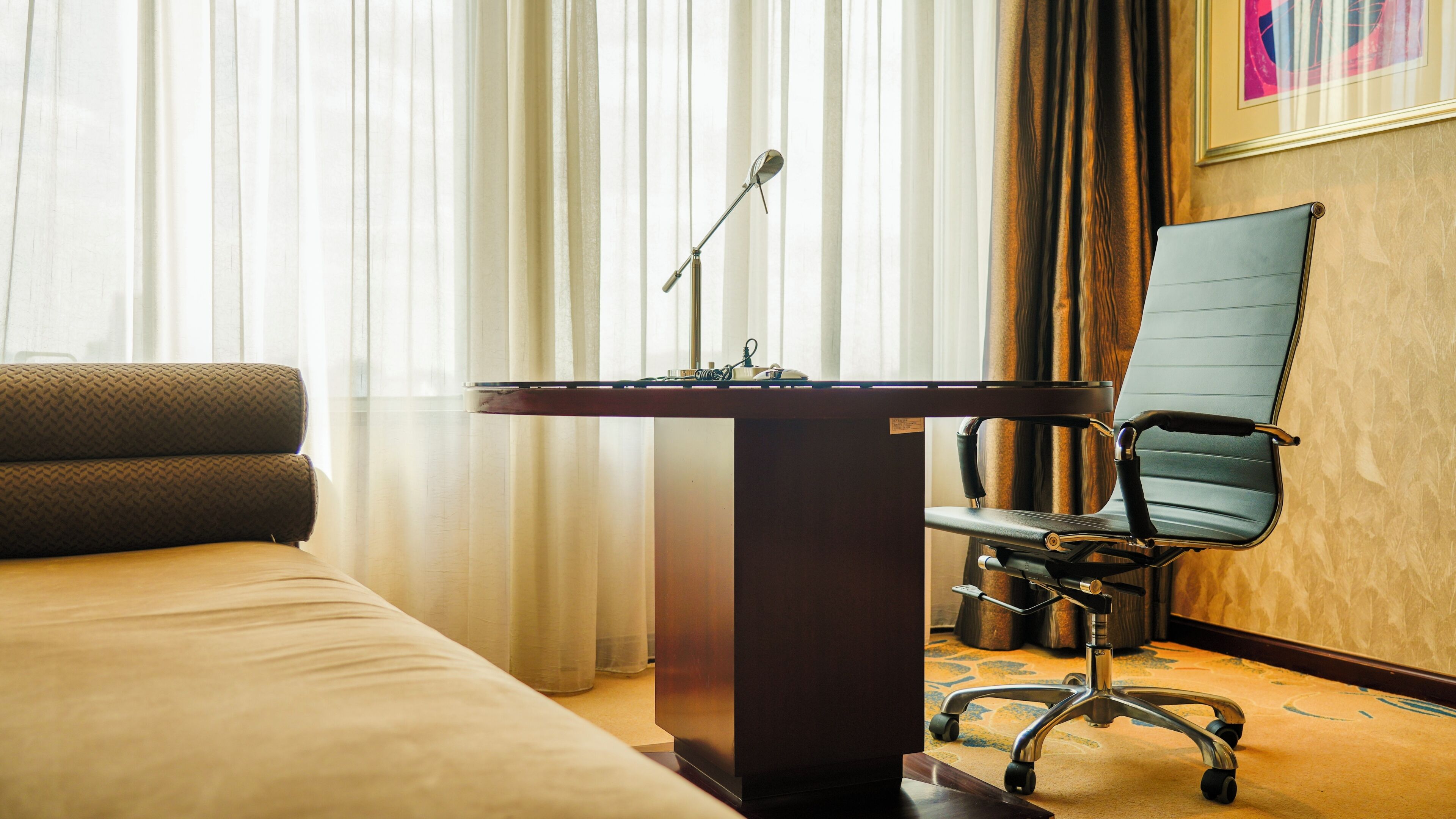 Habitació d'hotel amb un llit, un escriptori amb un micròfon, una cadira i una finestra amb cortines.