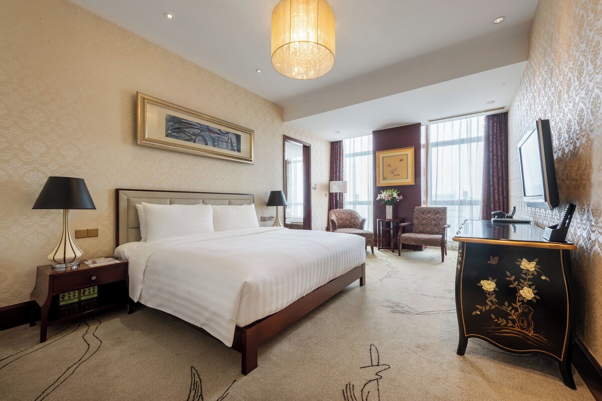 A hotel room with a large bed, a desk, a chair, and a television.