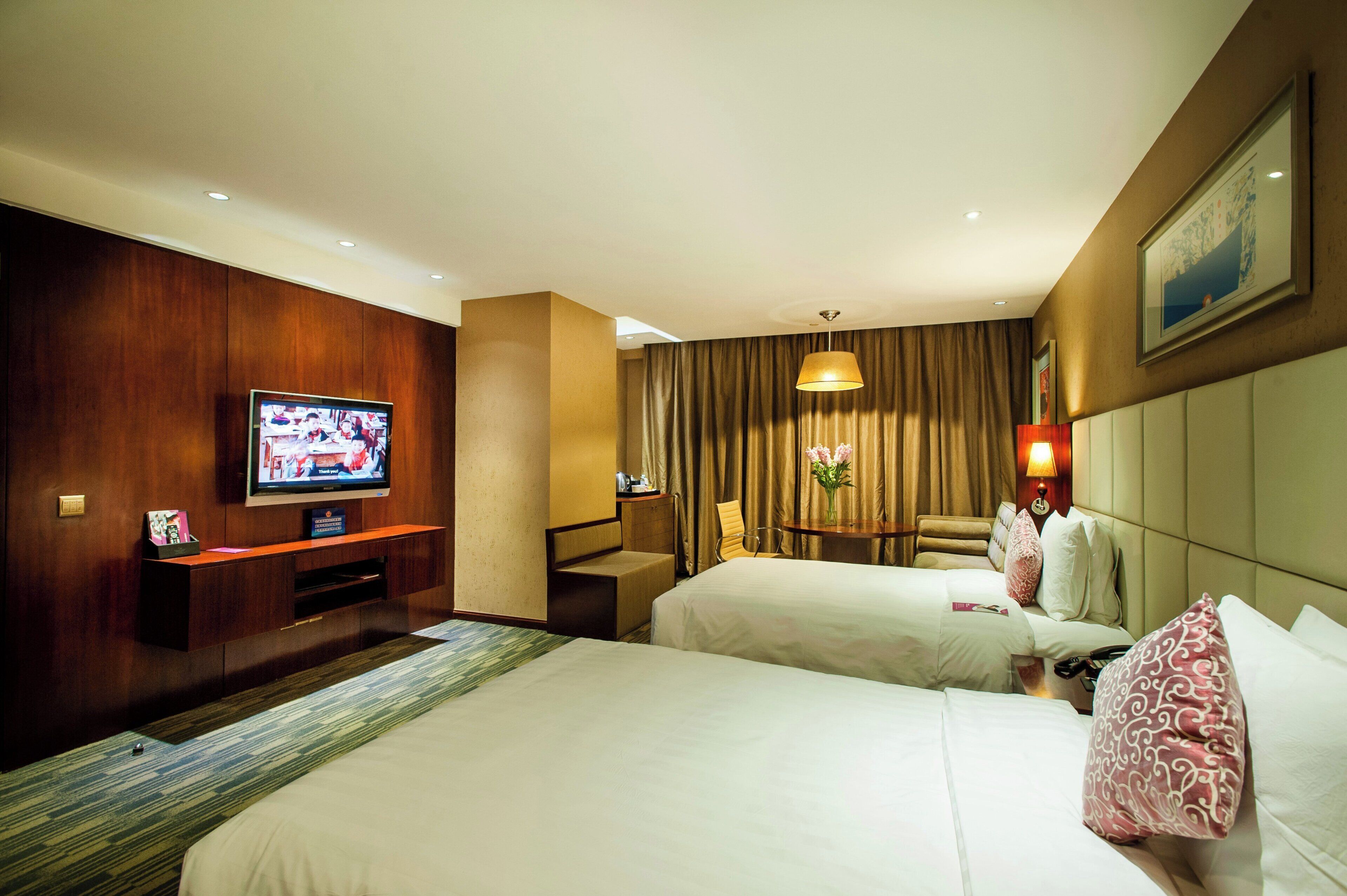 Habitación de hotel con dos camas, televisión, escritorio, silla y lámpara.