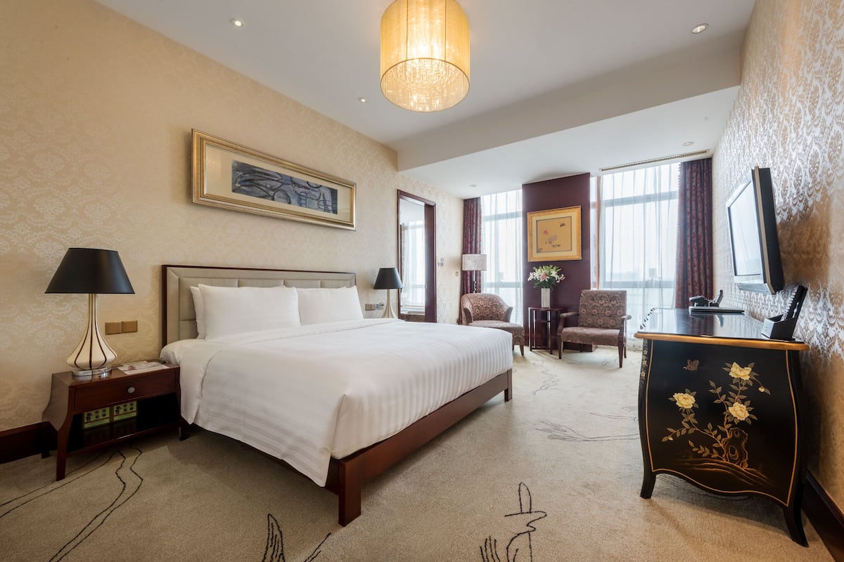 Ein Hotelzimmer mit einem großen Bett, einem Schreibtisch, einem Sessel und einem Fernseher.