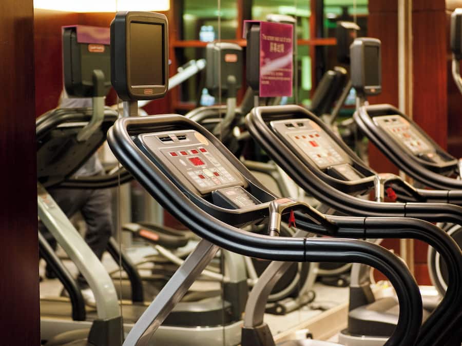 Varias bicicletas estáticas alineadas en un gimnasio, con paneles de control y un cartel sobre ellas.
