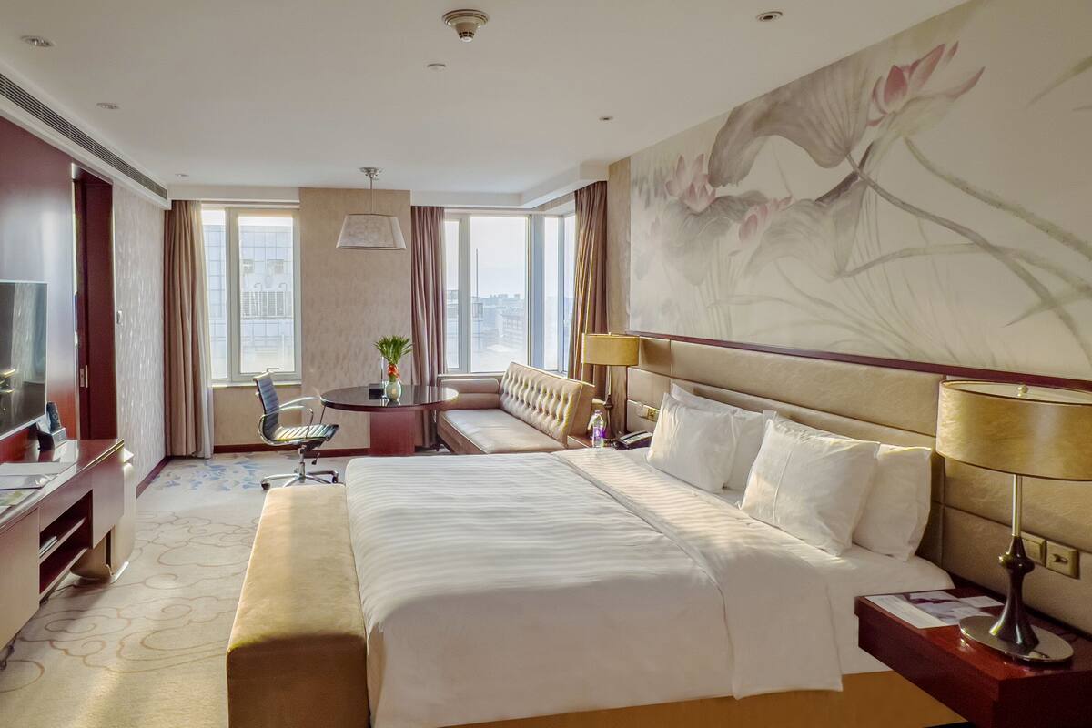 Ein Hotelzimmer mit einem großen Bett, einem Schreibtisch, einem Sessel, einem Fernseher und einem großen Fenster mit Vorhängen.