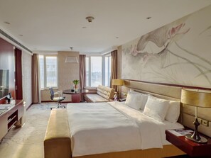 Habitación de hotel con una cama grande, un escritorio con una silla, un televisor y un ventanal amplio.