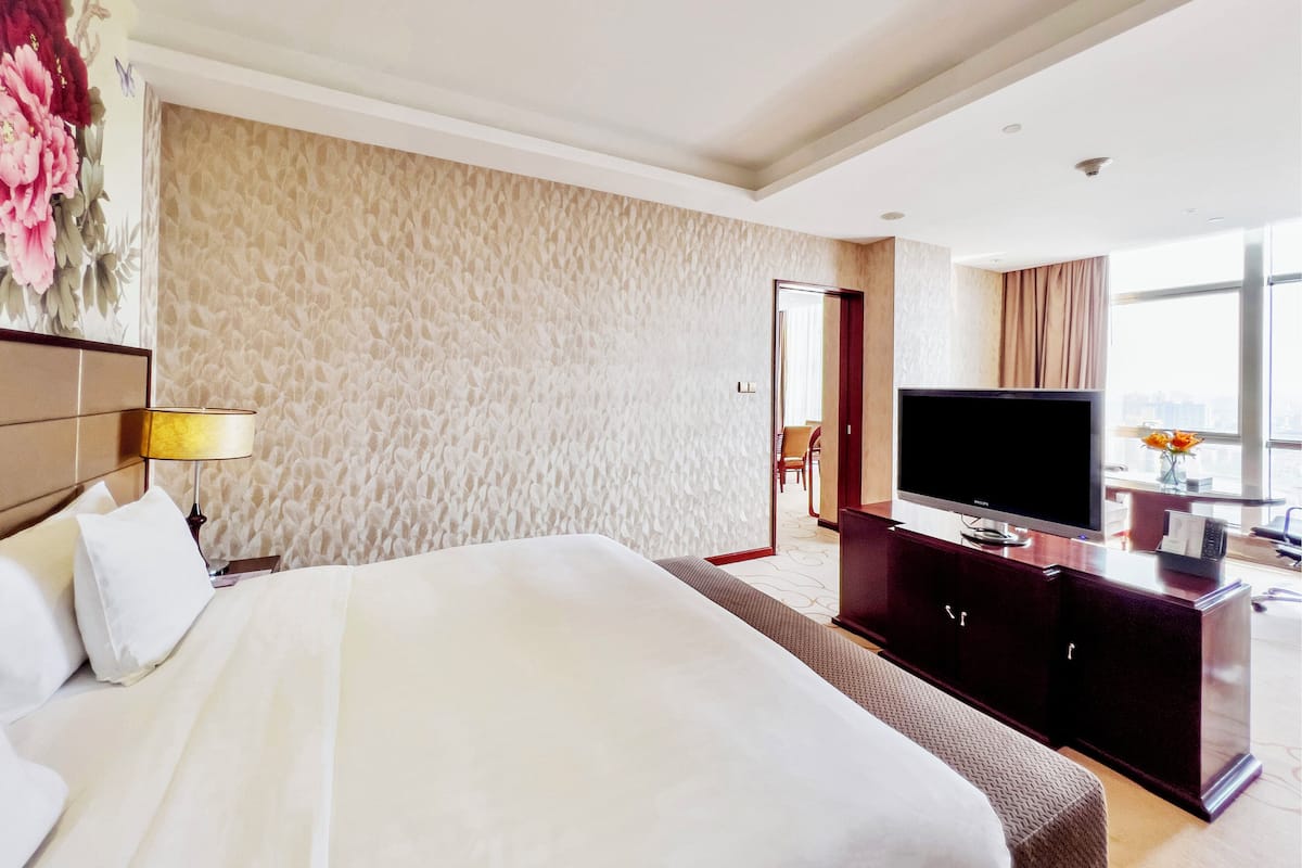 Ein Hotelzimmer mit einem großen Bett, einem Fernseher, einem Schreibtisch und Blick auf die Stadt durch das Fenster.