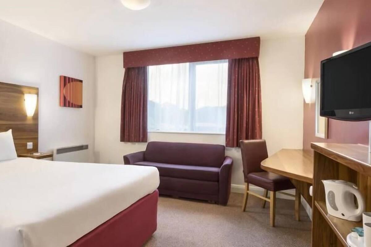 A hotel room with a large bed, a sofa, a desk, and a television.