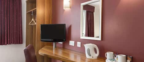 A hotel room with a wooden desk, a television, a mirror, and a coffee station.