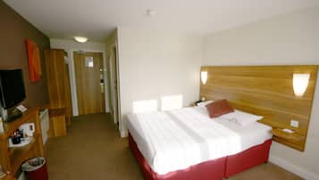 A hotel room with a large bed, a wooden headboard, a television, and a small desk with a chair.