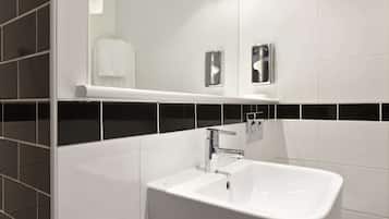 A modern bathroom with a white sink, chrome faucet, and a mirror above it. There are two towel dispensers on the wall.