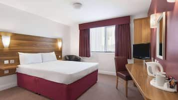 A hotel room with a bed, a desk, a chair, a television, and a window with curtains.