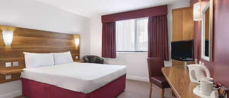 Habitación de hotel con cama, escritorio, silla, televisor y ventana con cortinas.