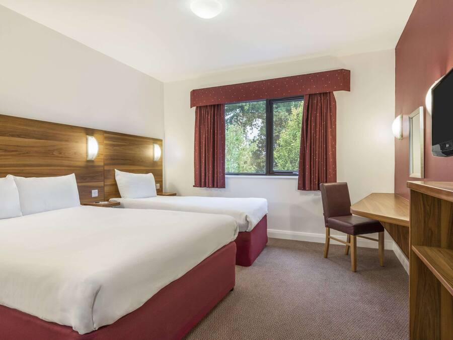 A hotel room with two beds, a desk, a chair, a TV, and a window with curtains.