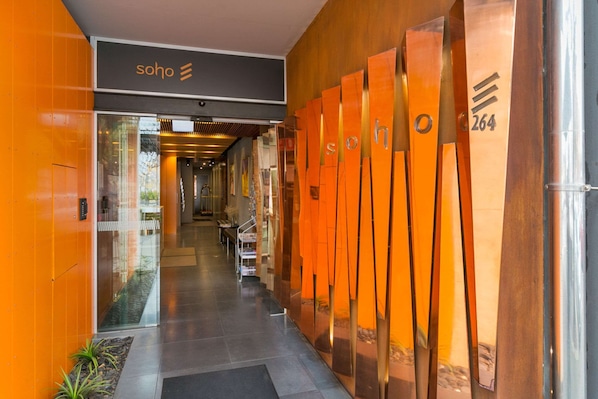 Entrada de hotel com design moderno, destacando uma porta de vidro, área de recepção e detalhes decorativos em tons de laranja.