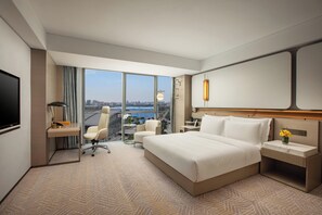 Habitación de hotel con una cama grande, un escritorio, una silla, un televisor y vistas de la ciudad.