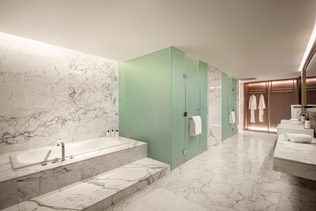 A modern bathroom with a marble sink, a large bathtub, and a green vanity.