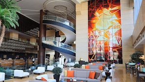 Un lobby de hotel moderno con una escalera espiral, varias zonas de estar y un gran mural abstracto.