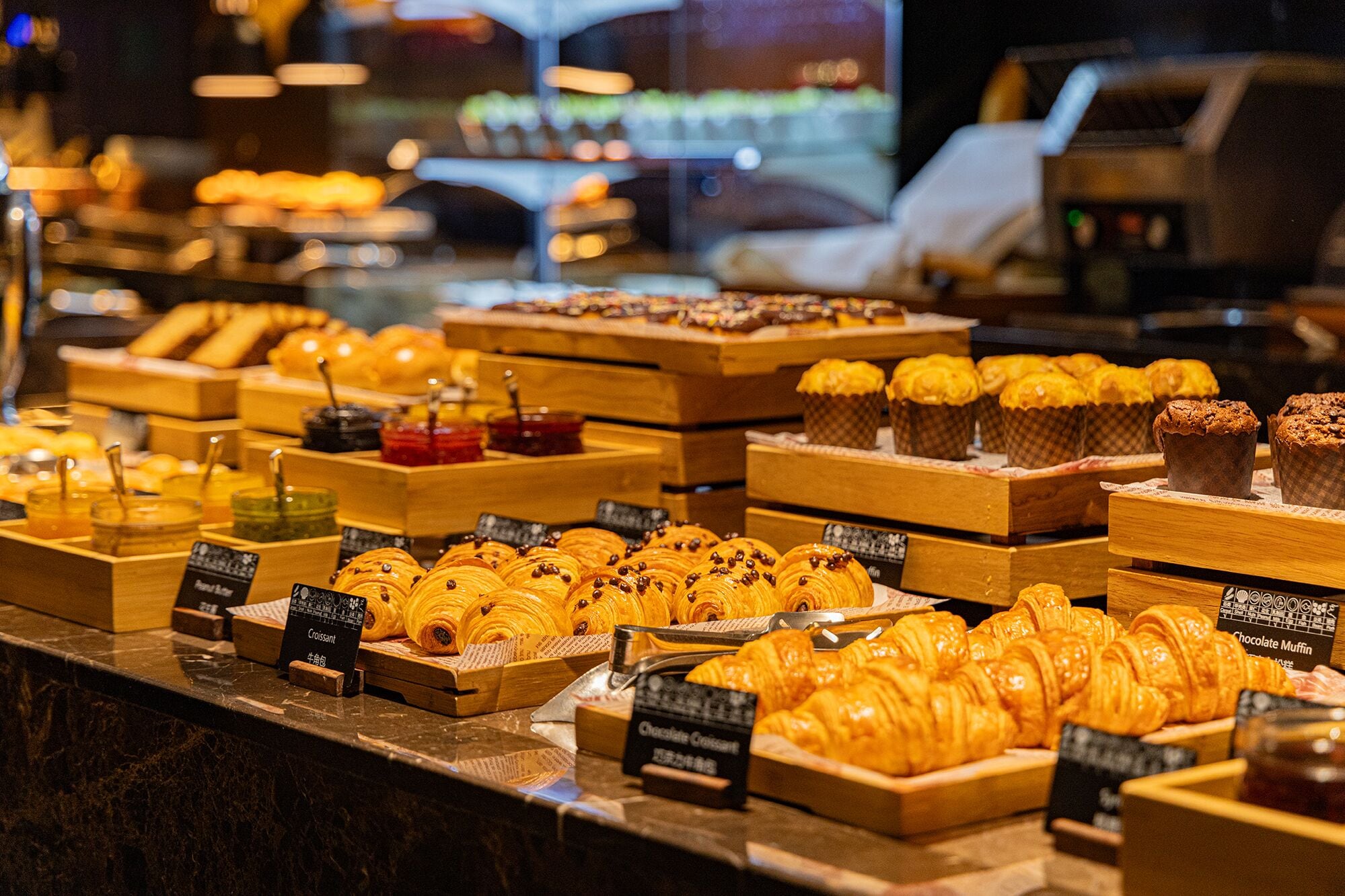 A bakery display with various pastries and baked goods, including croissants and muffins, arranged on wooden stands.