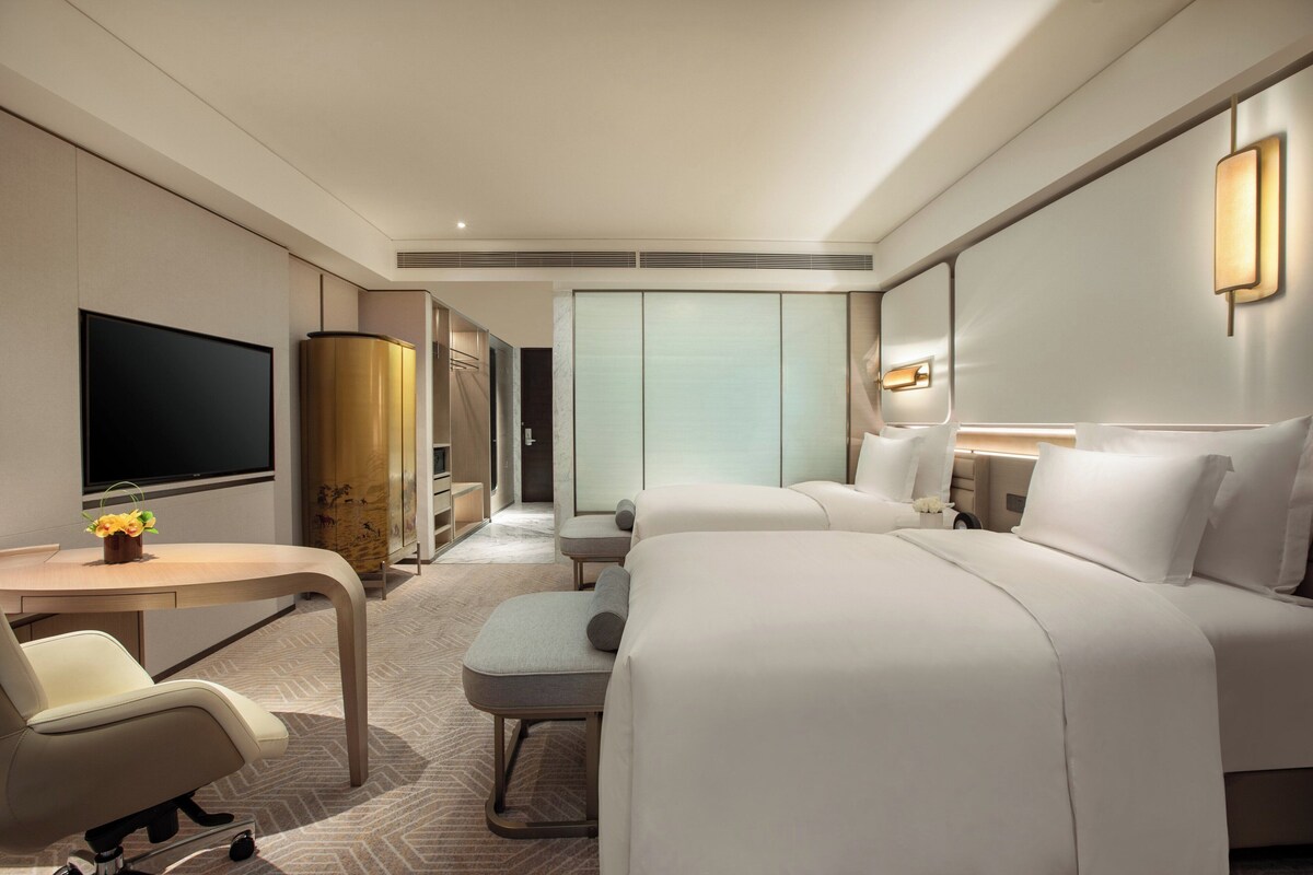 A hotel room with a bed, a desk with a chair, a television, and a wardrobe.