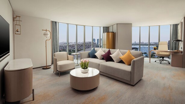 A modern hotel room with a large window offering a city view, a sofa with colorful cushions, a round coffee table with a vase, and a desk with a chair. - InterContinental Beijing Beichen by IHG (Beijing)