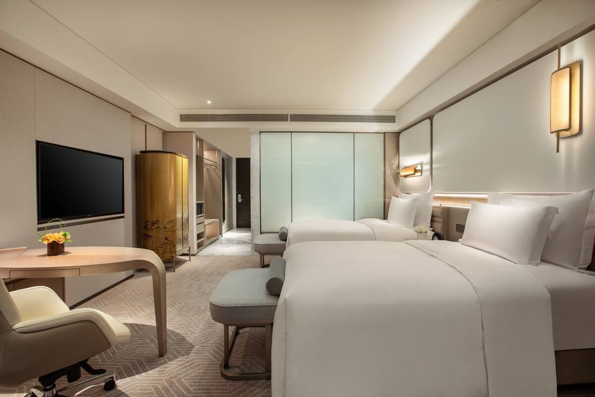 A hotel room with a bed, a desk with a chair, a television, and a wardrobe.