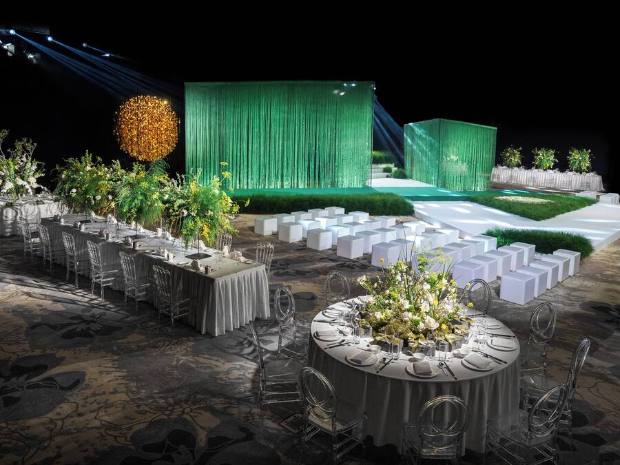 A formal outdoor event setup with round tables, clear chairs, and green curtains.