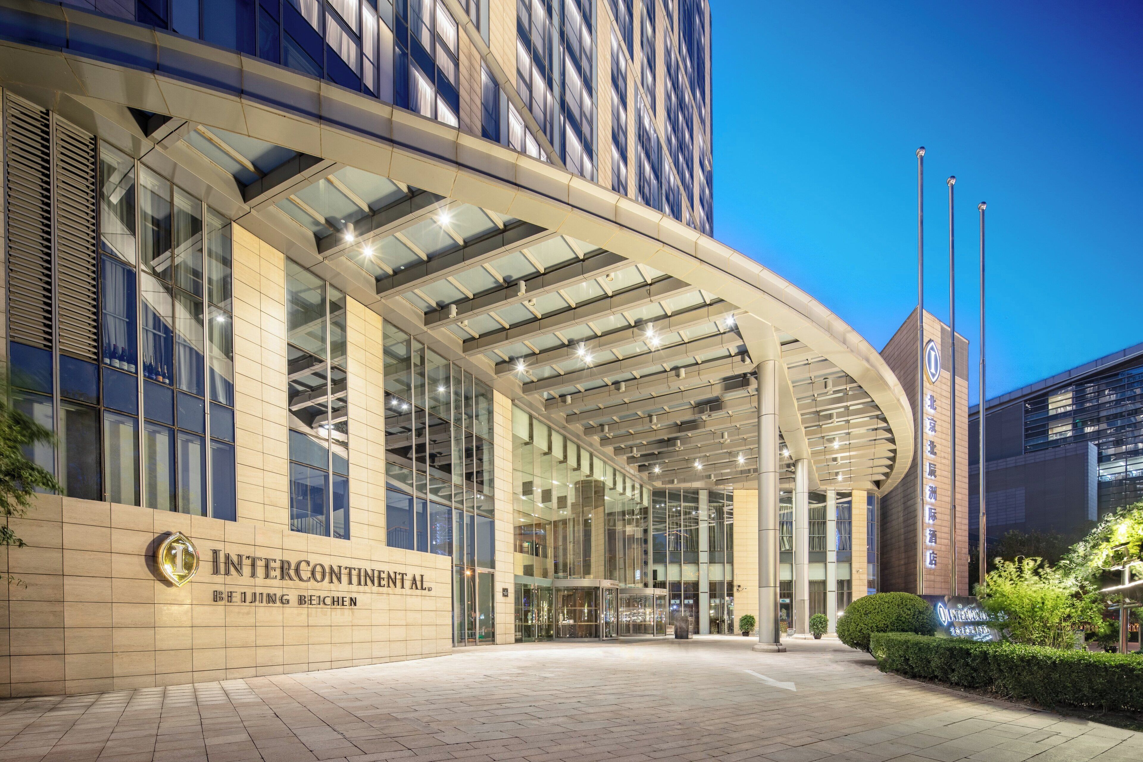 Entrada moderna de un hotel con fachada de vidrio, un voladizo curvo y un letrero que indica que es una sucursal de InterContinental en Beijing.