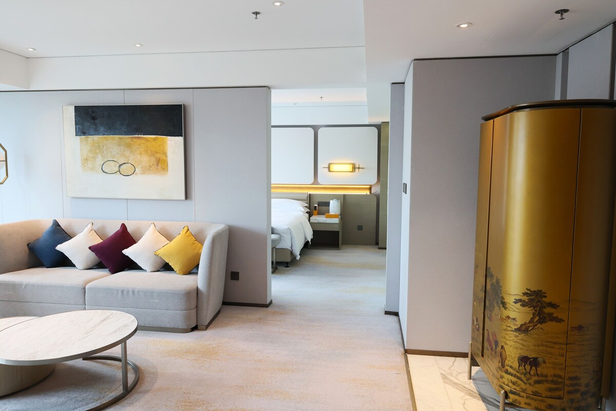 A modern hotel room with a sofa, a round table, and a large decorative piece.