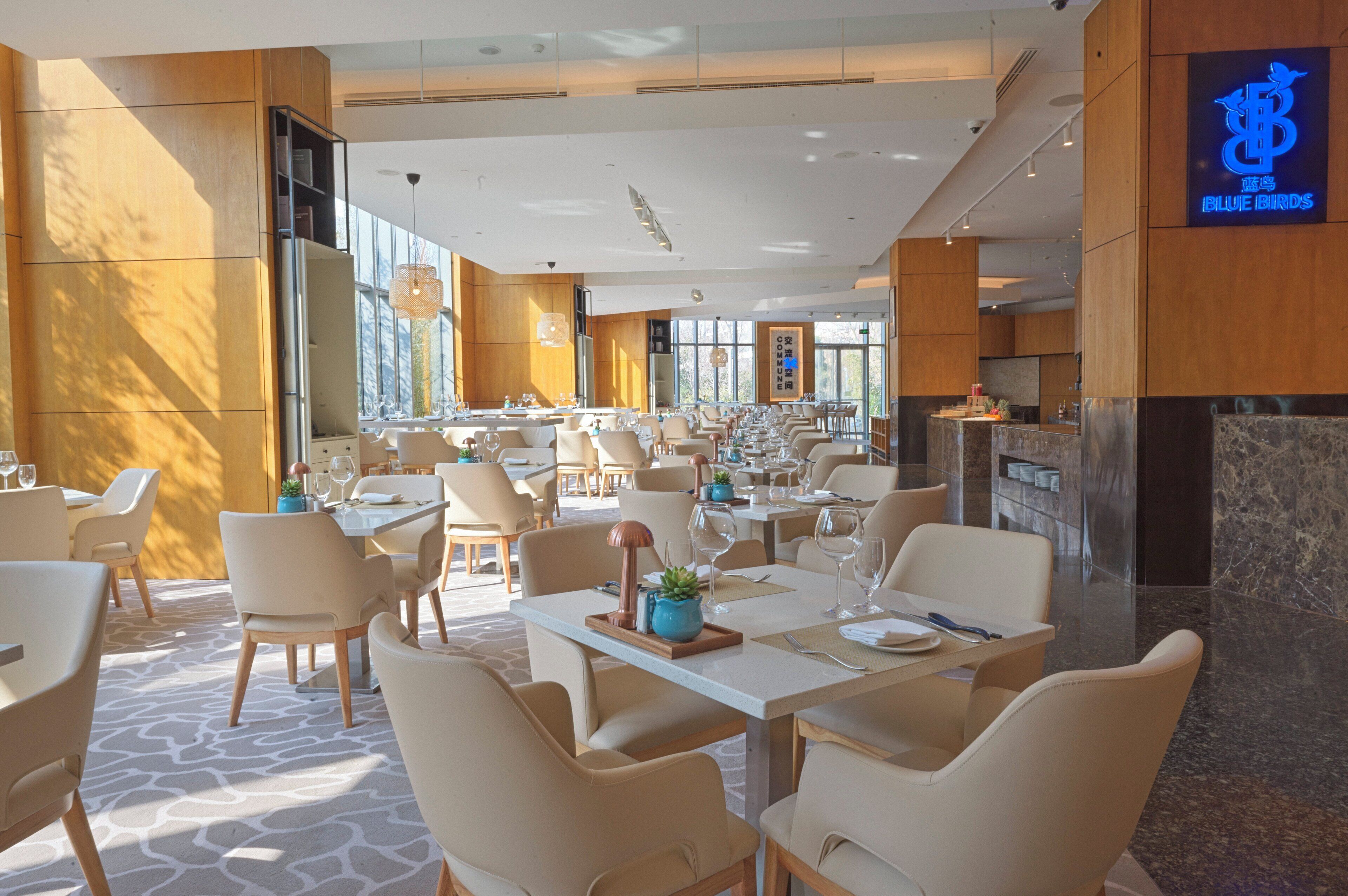 A spacious restaurant with multiple dining tables and chairs, large windows allowing natural light, and a modern interior design.