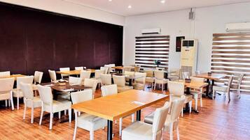 A spacious dining area with multiple tables and chairs, air conditioning units, and a large dark wall.
