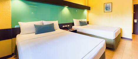 A hotel room with two beds, each with white linens and a single pillow. The room has a green accent wall and a black headboard.