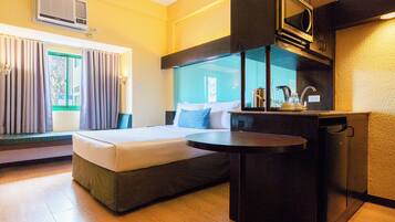 A hotel room with a bed, a small table, a kitchenette, and a window with curtains.