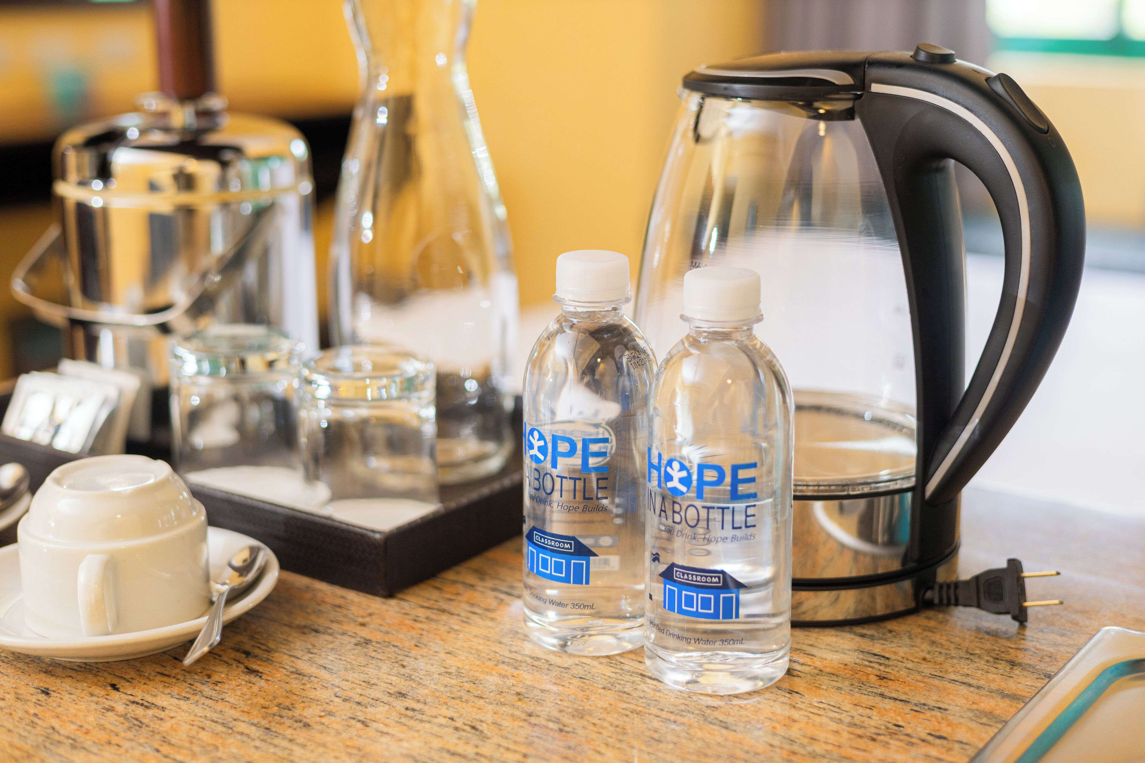 A kitchen area with a coffee maker, two water bottles labeled "PE NABOTTLE," and a cup on a saucer.