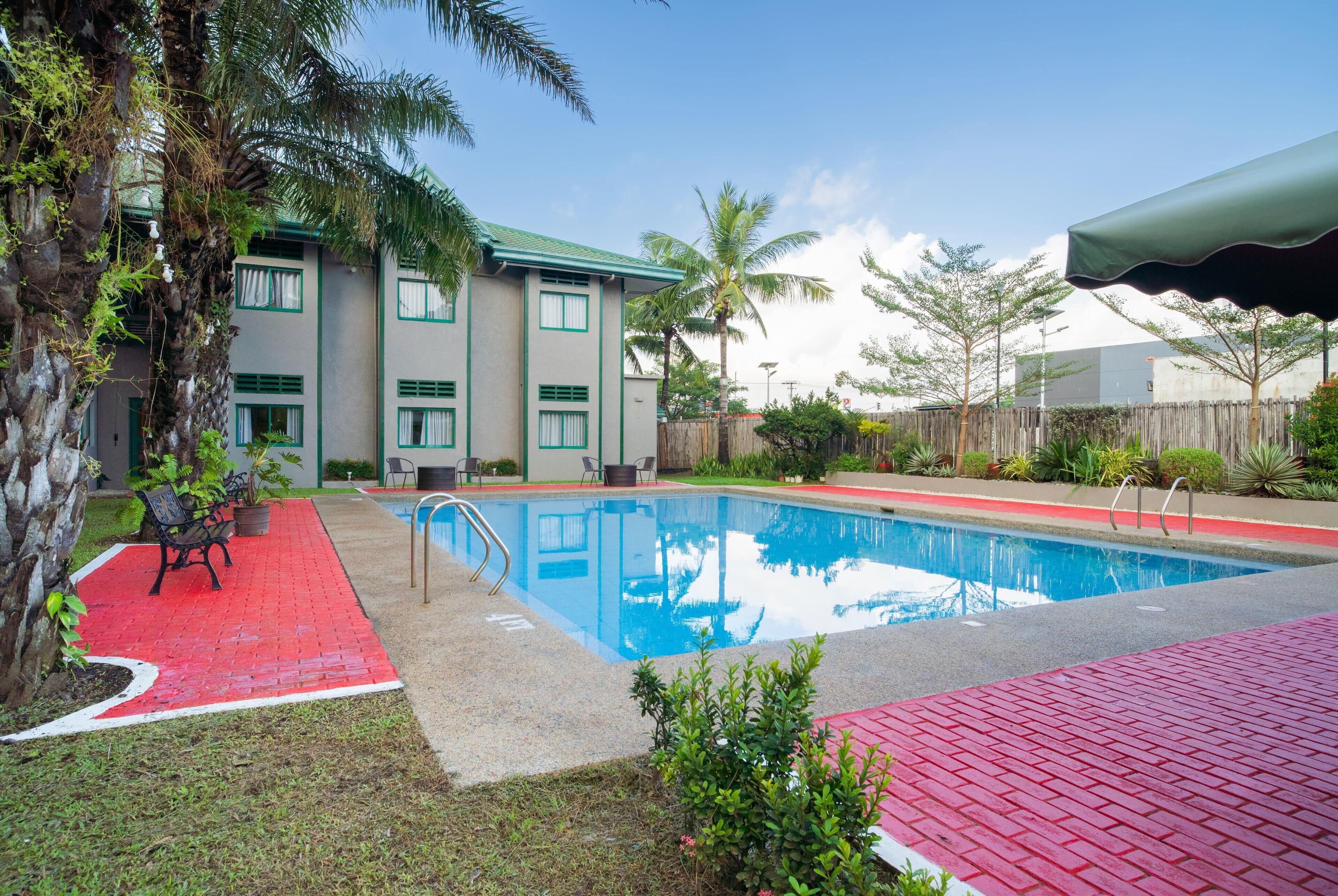 Una piscina con cubierta roja, un edificio con detalles verdes y palmeras.