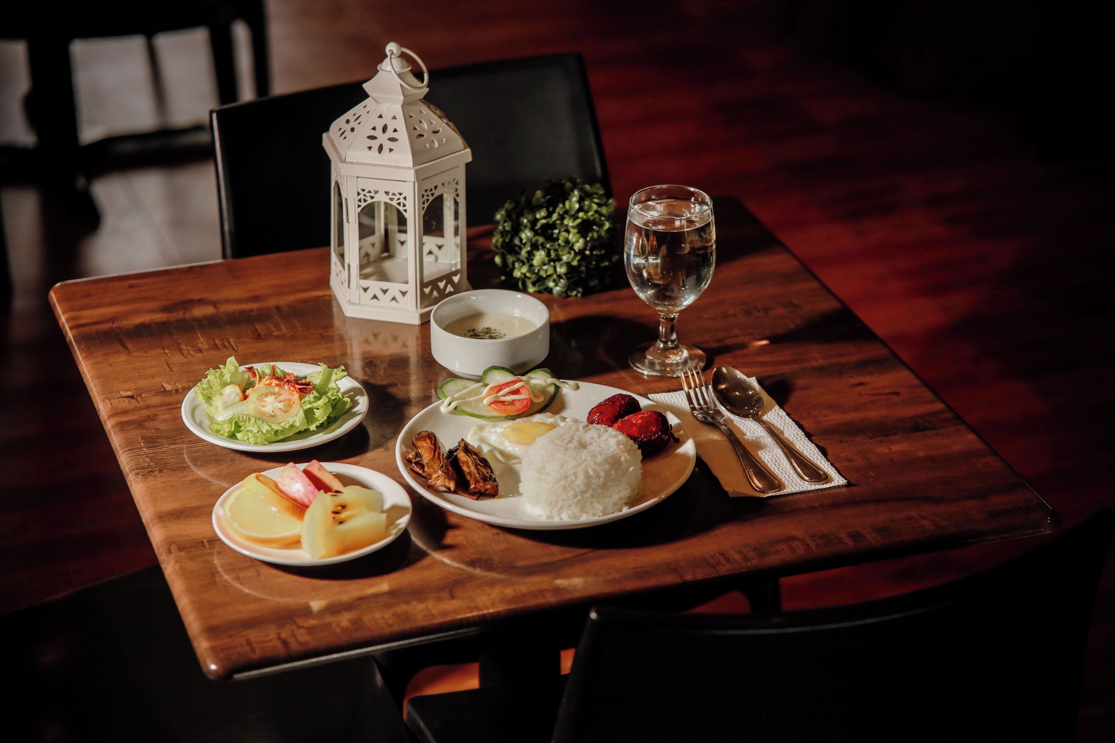 A dining table with plates of food, a glass of water, and a white lantern.