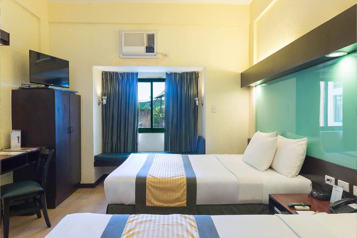 Ein Hotelzimmer mit Bett, Schreibtisch, Stuhl, Fernseher und einem Fenster mit Vorhängen.