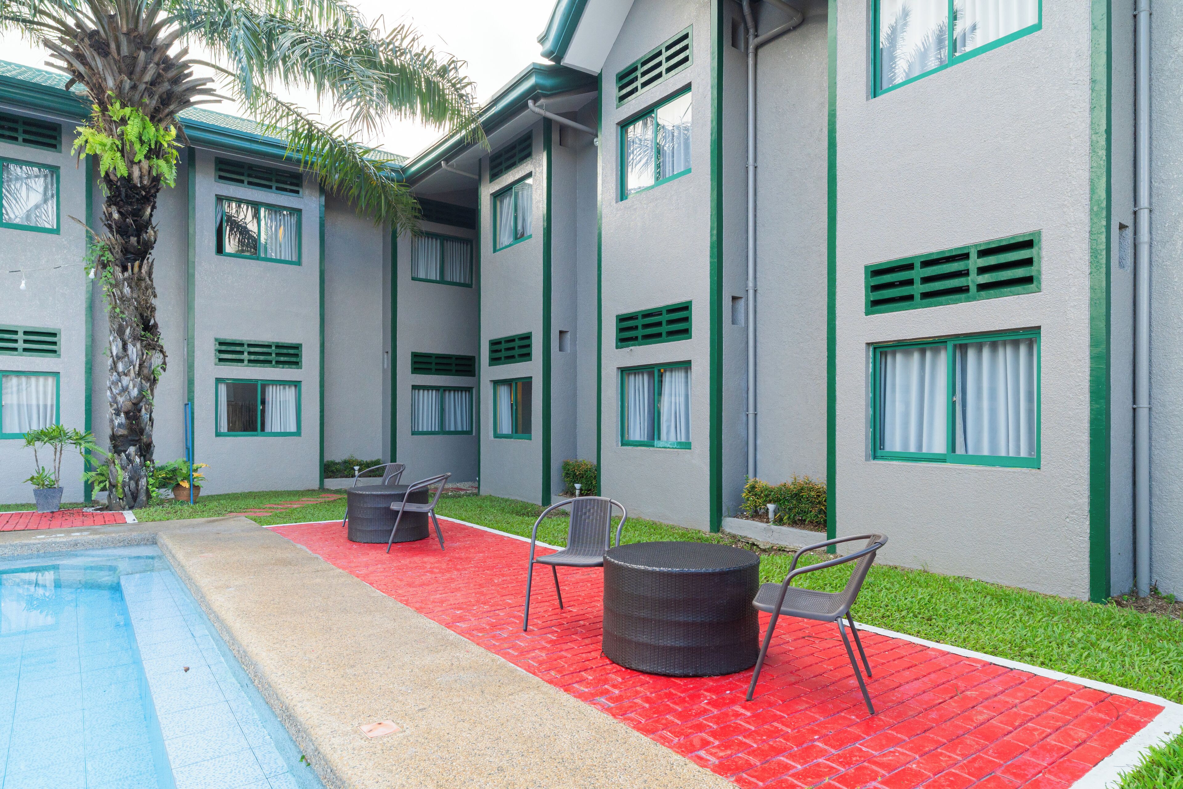 A hotel courtyard with a swimming pool, outdoor seating, and a palm tree.