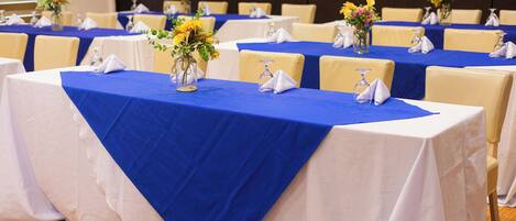 A conference room with tables set for a meeting. Each table has a blue tablecloth, white napkins, and a vase with flowers.