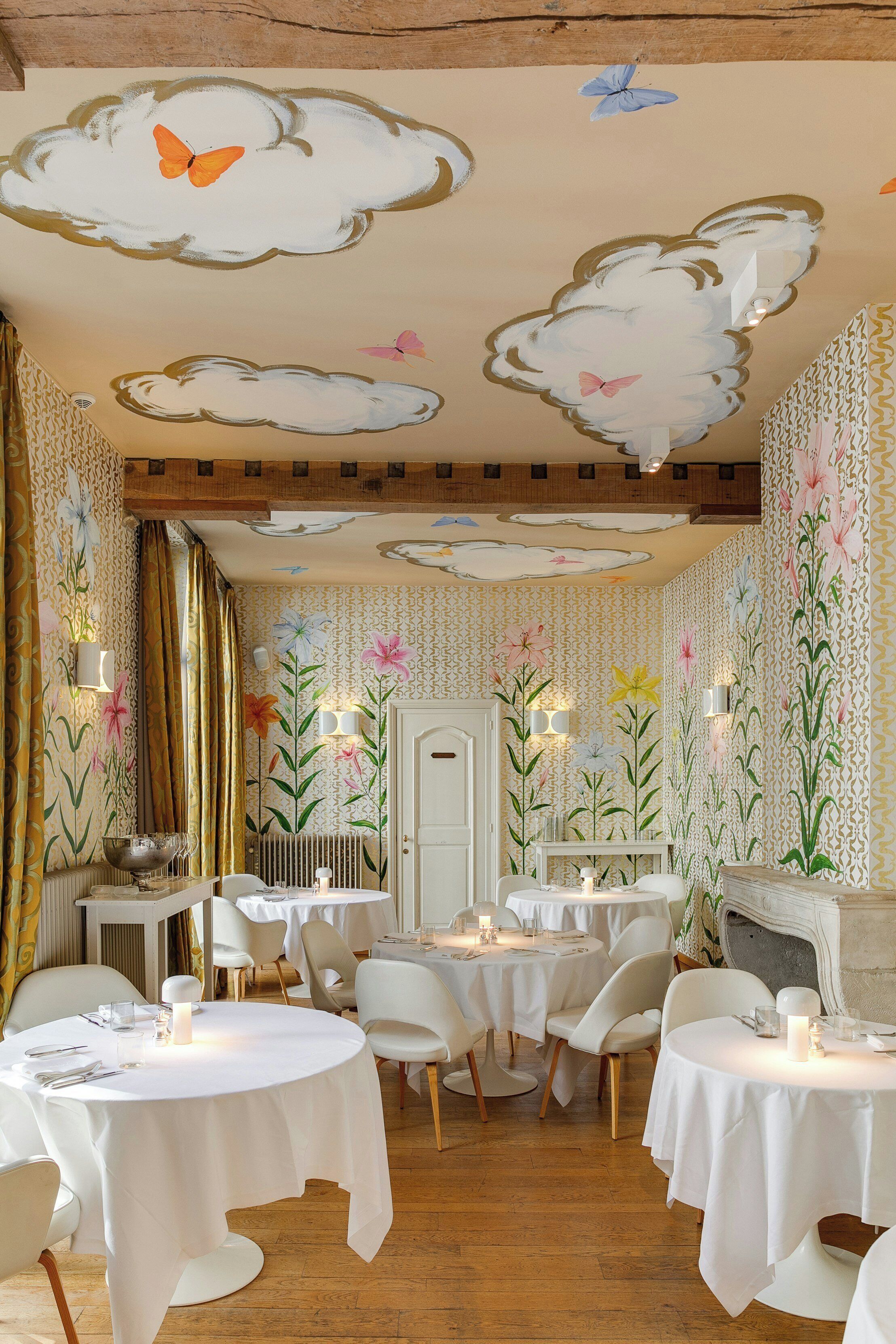 A dining area with round tables, white chairs, and floral wall decorations.