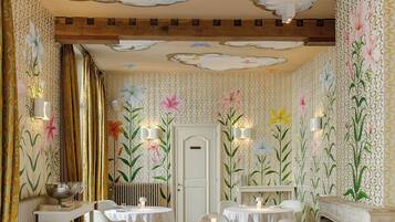 A dining area with round tables, white chairs, and floral wall decorations.