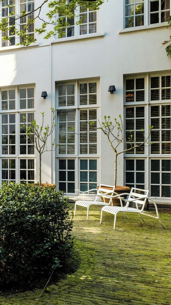 Un bâtiment doté de grandes fenêtres, d’une cour pavée et d’un banc en métal blanc.