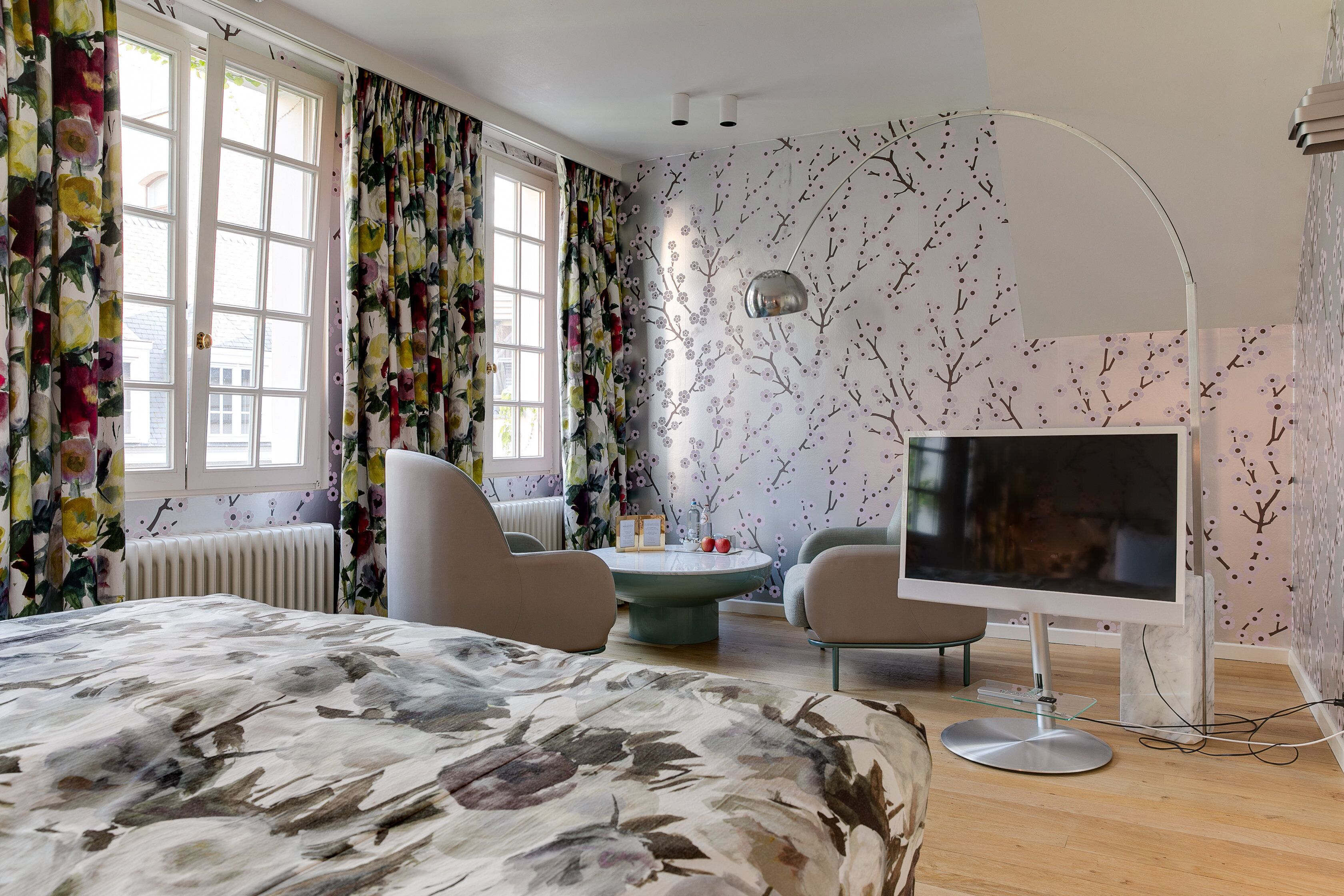 Un dormitorio con una cama, dos sillas, un televisor y una mesa con un jarrón.