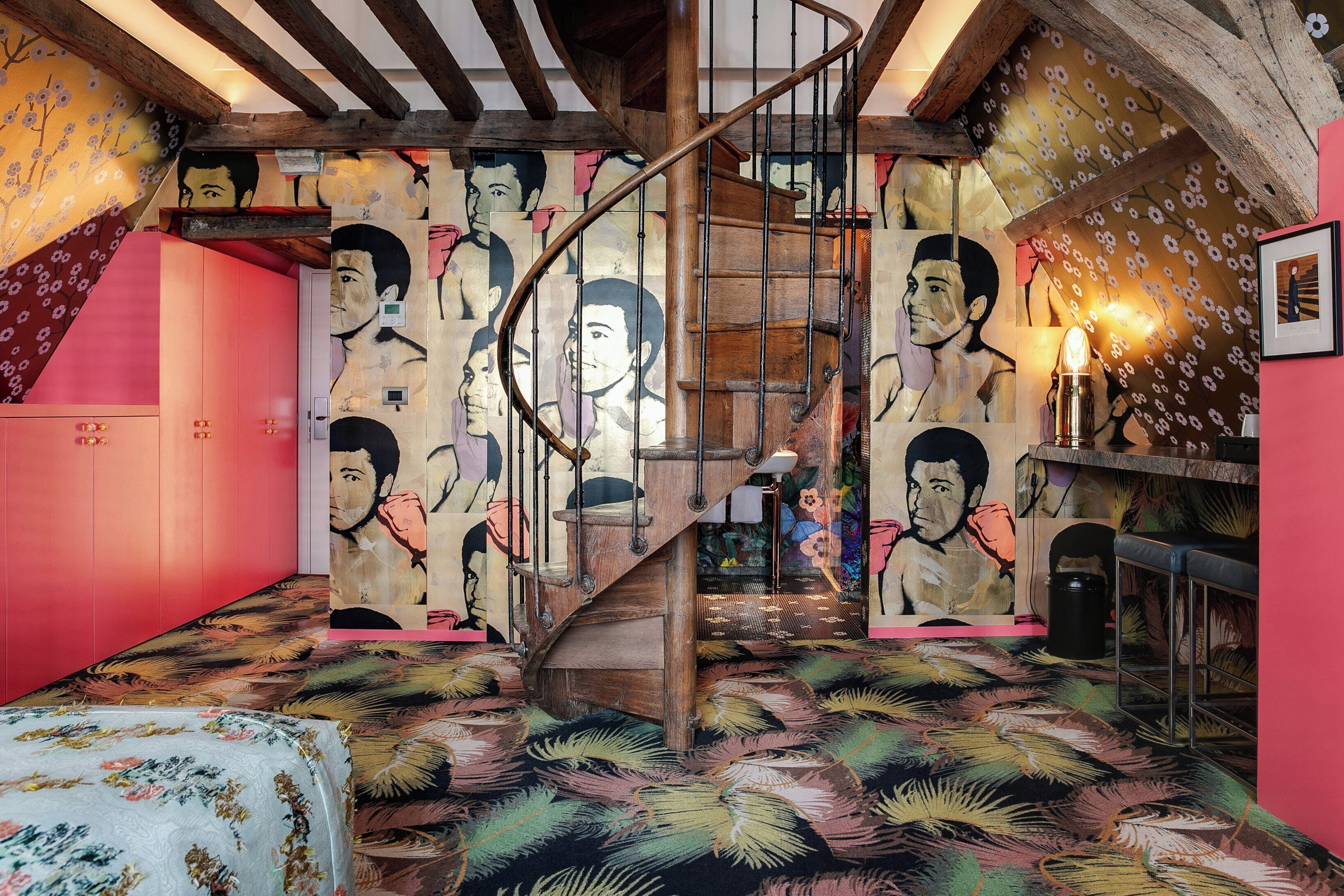 Una habitación con escalera de caracol, cama con ropa de cama floral y un mural grande en la pared.