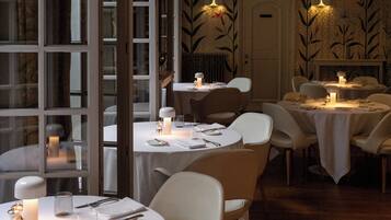 Un restaurante con mesas redondas, sillas blancas y un ambiente a la luz de las velas.