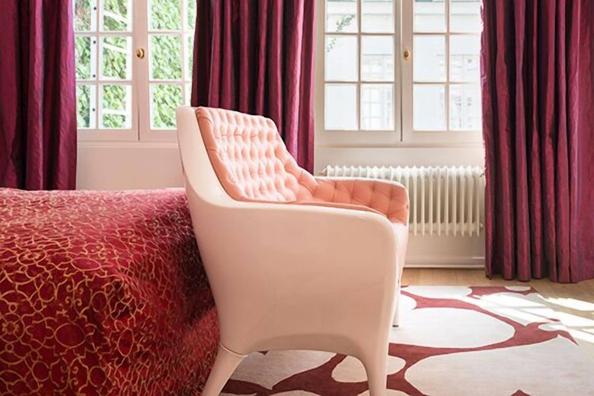 A room with a bed, a chair, a desk, and a window with curtains.