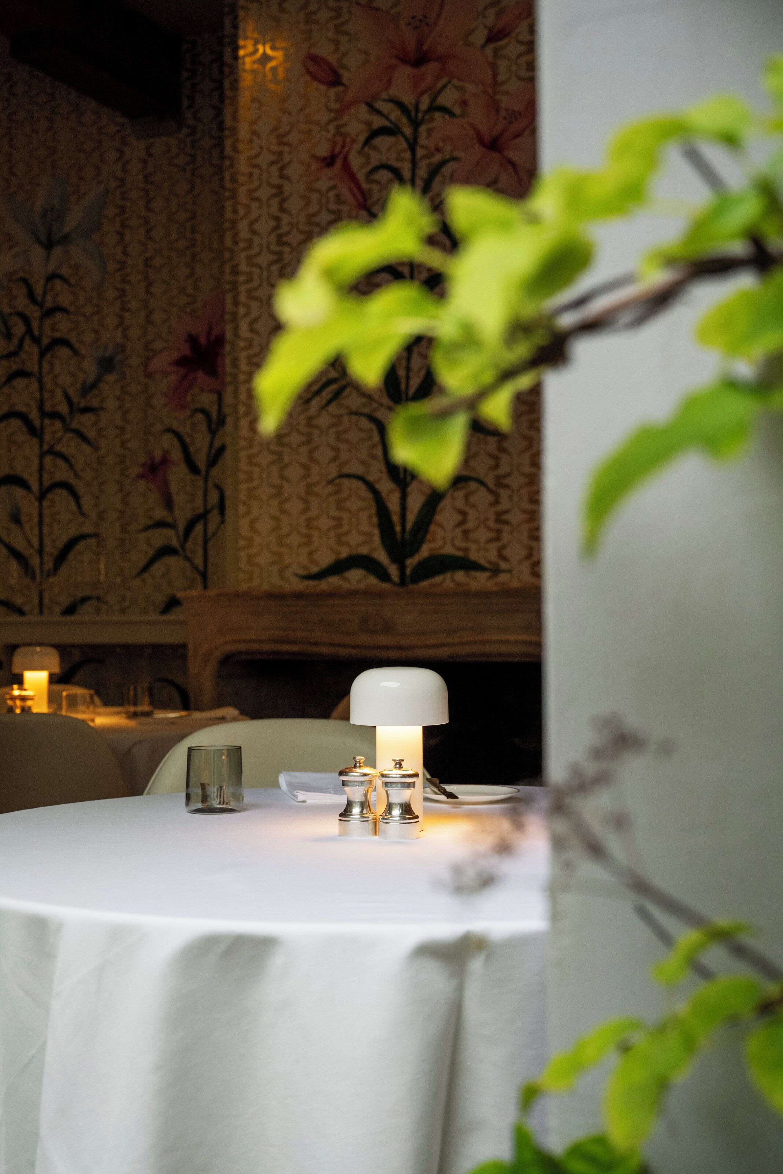 A dining table with a white tablecloth, a lit lamp, and a glass of water.