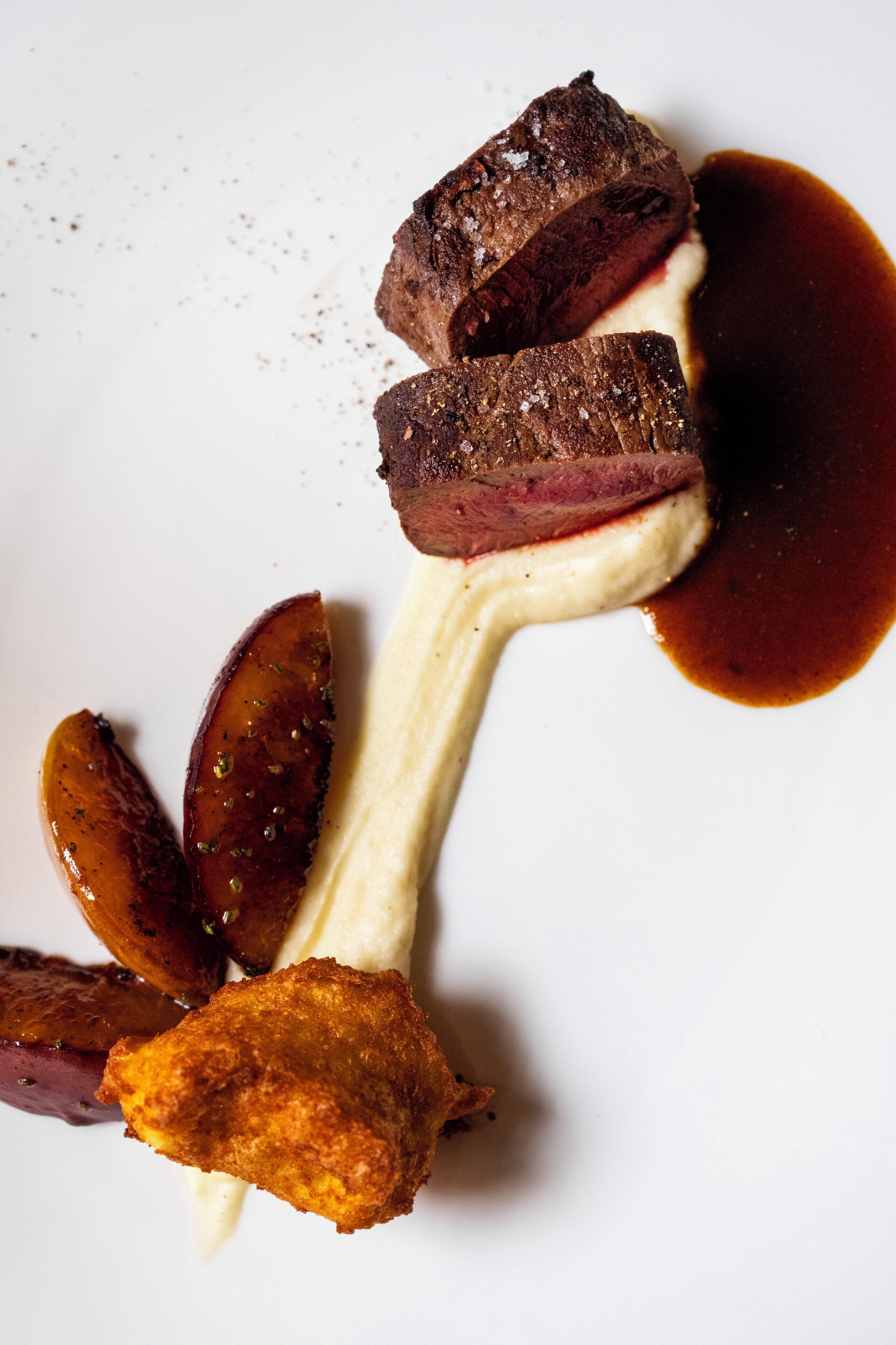 A dish with steak, potatoes, and a creamy sauce on a white plate.