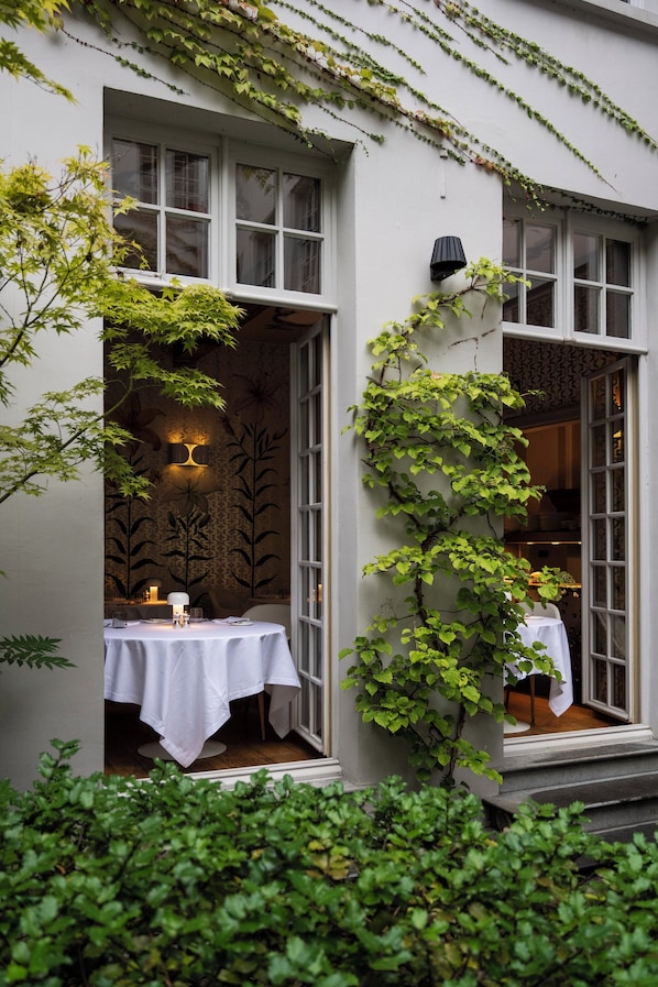A building with ivy-covered walls, a dining area with a table and chairs, and a staircase leading to an upper level.