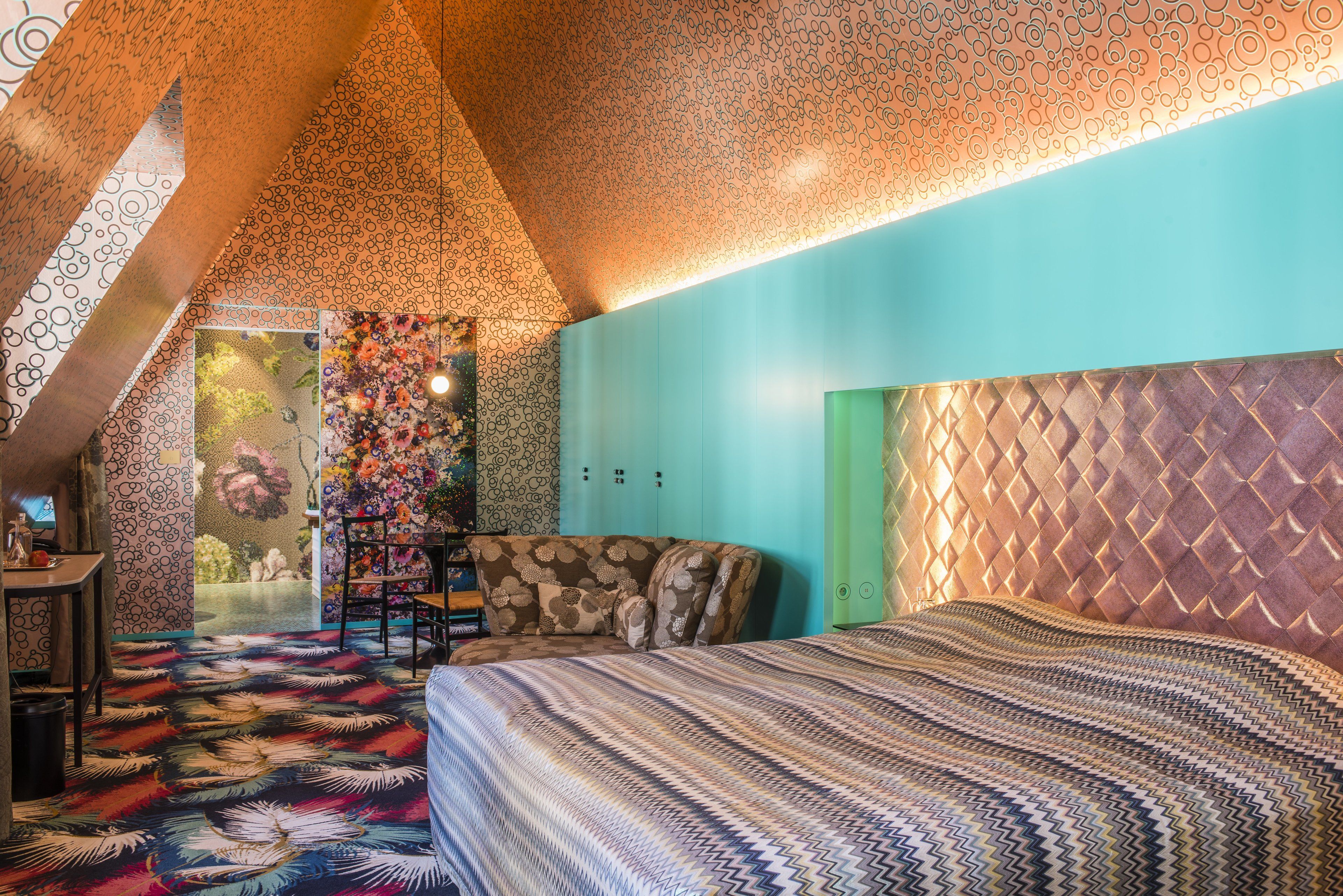 Een slaapkamer met een kamerbedekking met een patroon, een bed met een strepenbed overtrek, een stoel en een kledingkast.