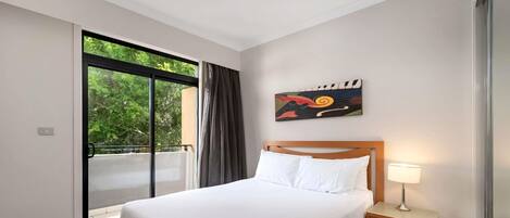 A hotel room with a bed, a nightstand, a lamp, a painting, and a sliding glass door leading to an outdoor area.